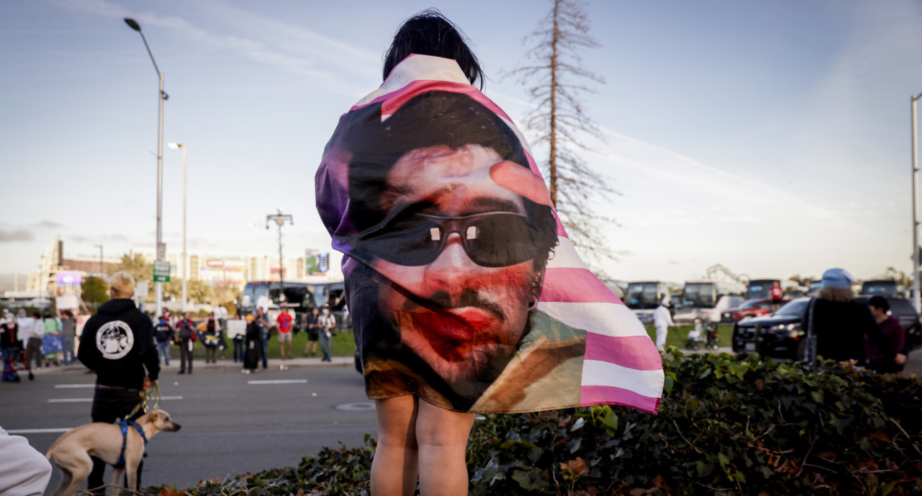 Ο Bad Bunny απεικονισμένος πάνω σε σημαία των ΗΠΑ αγκαλιάζει την πλάτη θαυμάστριάς του πριν το Super Bowl LX / Πηγή: Brontë Wittpenn / San Francisco Chronicle via Getty Images