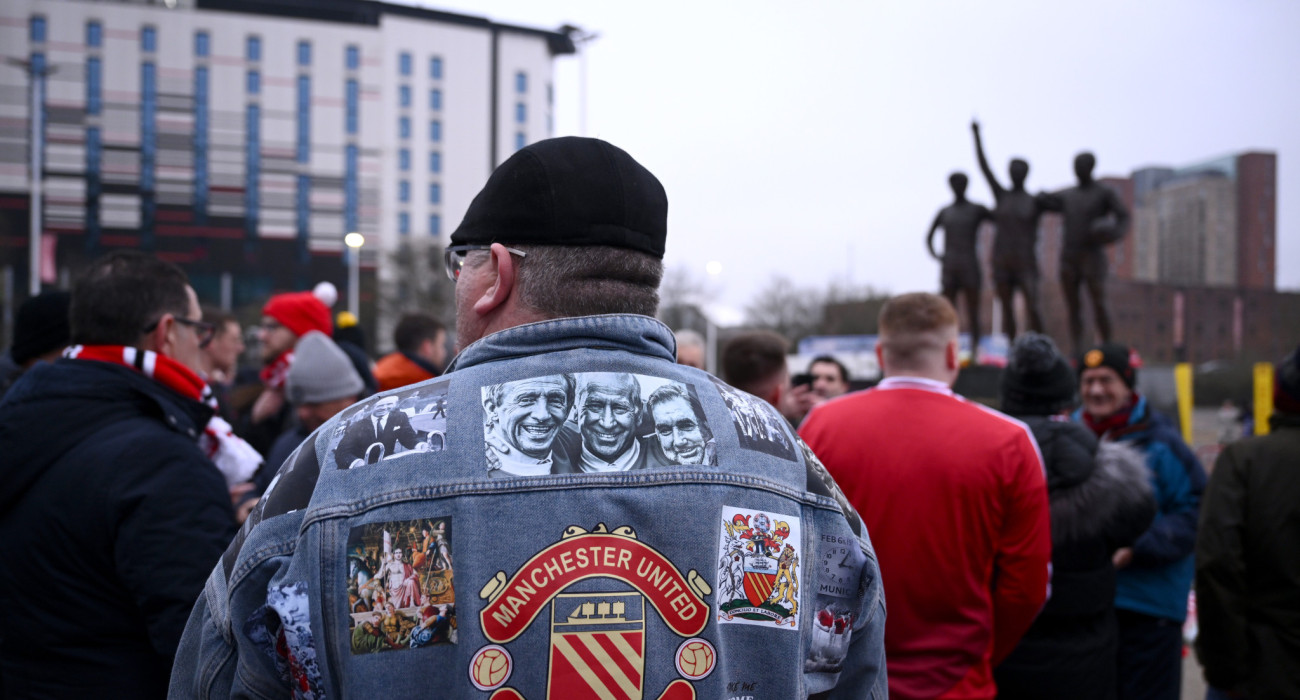 Οπαδός της Γιουντάιτεντ με ένα θρυλικό τζάκετ που απεικονίζει τους Τζορτζ Μπεστ, Μπόμπι Τσάρλτον και Ντένις Λο / Πηγή: Stu Forster / Getty Images